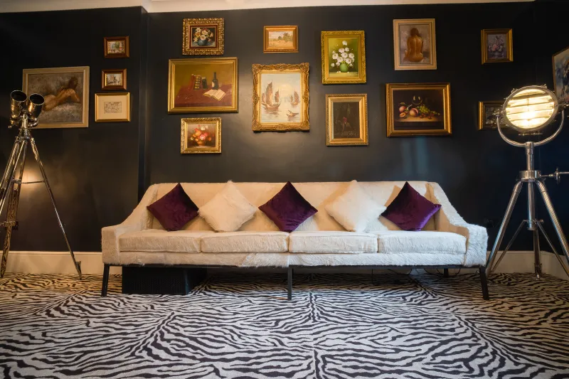 The parlour at CuVée VIII: a white sofa, purple cushions, gold-framed paintings and a zebra rug