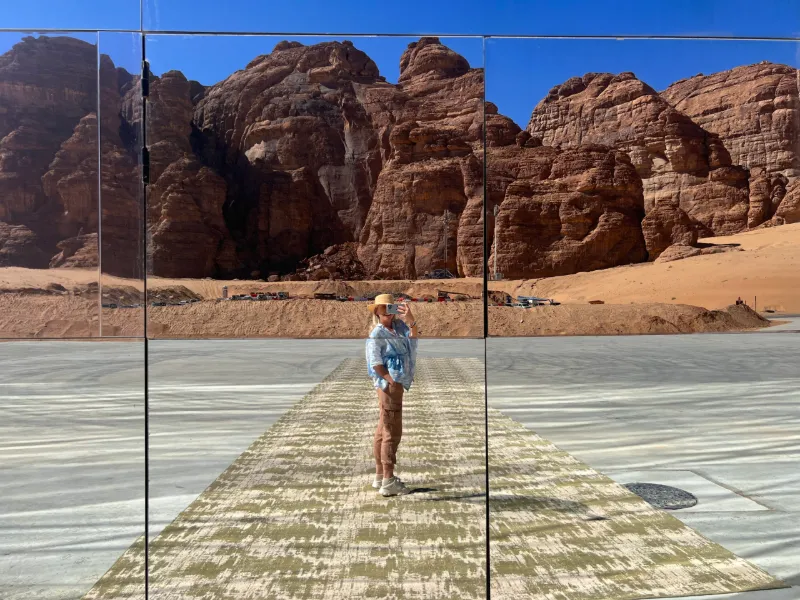 A figure on a mirrored walkway in a desert canyon