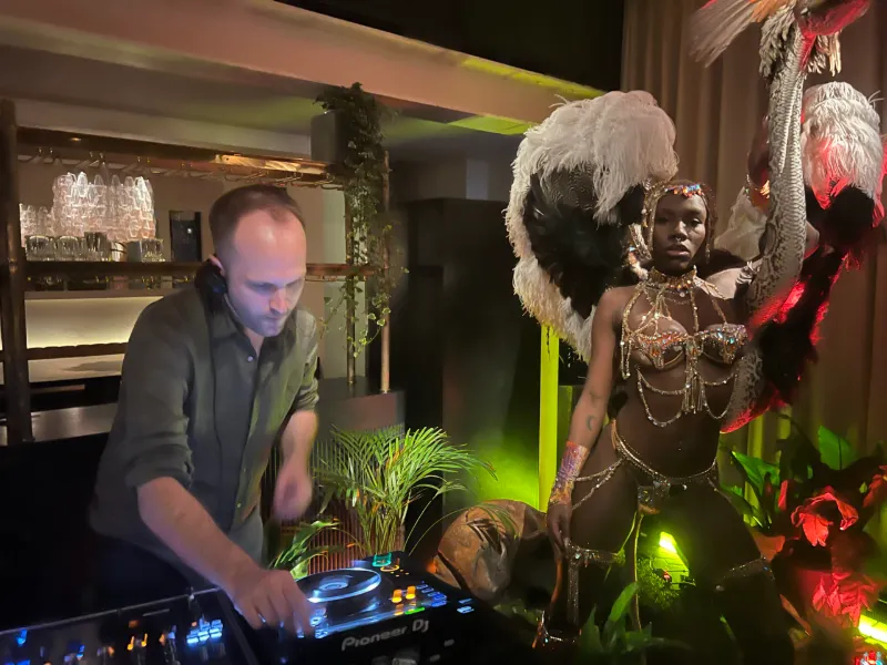 A DJ beside a feathered carnival performer