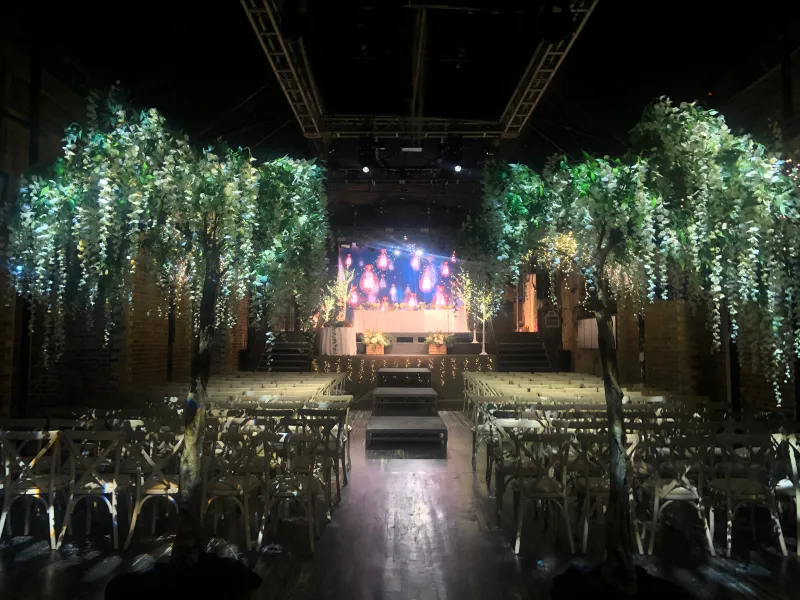 An indoor venue dressed with blossom trees, rows of chairs and a stage screen
