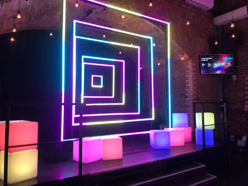 A neon square-tunnel light installation with glowing cubes under brick arches