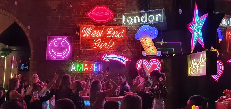 A neon wall reading “West End Girls”, “London”, “Amaze” and a smiley
