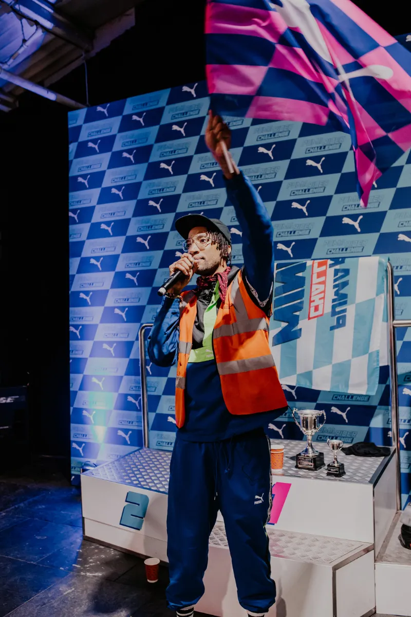 A performer with a chequered flag on the podium at a PUMA launch event
