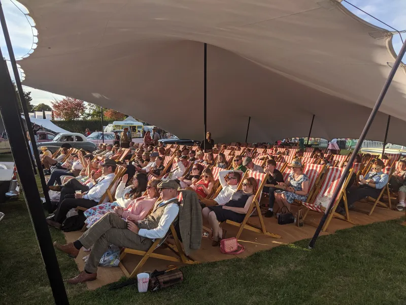 A deckchair audience in period dress under a stretch tent, Sky Cinema at the Goodwood Revival