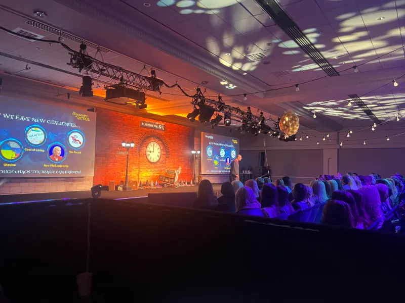 A themed conference stage with a clock and a brick-wall set, and projection on the ceiling